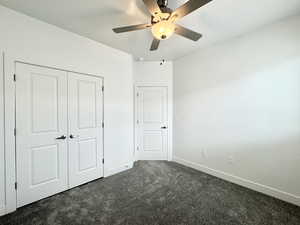 Unfurnished bedroom featuring baseboards, a ceiling fan, dark colored carpet, and a closet