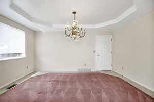 Carpeted empty room with an inviting chandelier, ornamental molding, visible vents, and a raised ceiling