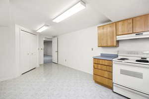 Kitchen with electric range, baseboards, under cabinet range hood, and light floors