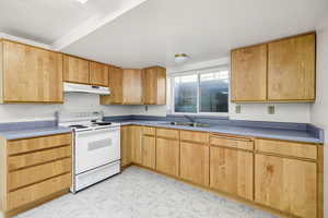 Kitchen featuring light floors, under cabinet range hood, a sink, and electric stove