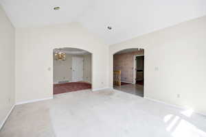Empty room featuring visible vents, arched walkways, baseboards, carpet flooring, and a notable chandelier