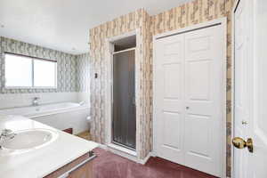 Bathroom featuring wallpapered walls, a shower stall, vanity, a closet, and a garden tub