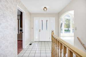 Foyer entrance featuring arched walkways, visible vents, baseboards, wallpapered walls, and light tile patterned floors