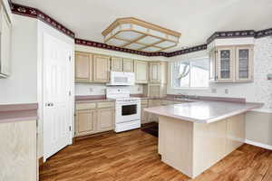 Kitchen with a peninsula, light wood-type flooring, wallpapered walls, glass insert cabinets, and white appliances