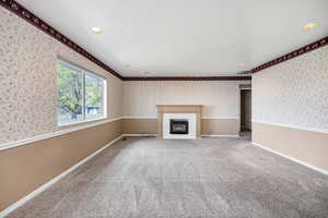Unfurnished living room featuring wallpapered walls, a glass covered fireplace, carpet, baseboards, and ornamental molding