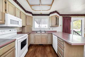 Kitchen with a sink, wallpapered walls, light brown cabinetry, white appliances, and a peninsula