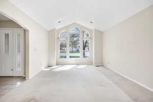 Carpeted spare room with arched walkways, vaulted ceiling, tile patterned floors, and baseboards