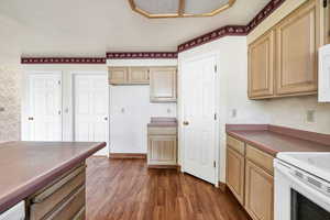 Kitchen with wallpapered walls, white appliances, light brown cabinetry, and dark wood-style flooring