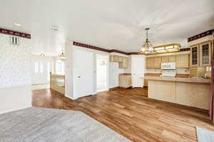 Kitchen featuring an inviting chandelier, light wood-type flooring, white microwave, glass insert cabinets, and range