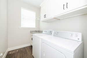 Clothes washing area with visible vents, dark wood-type flooring, baseboards, washer and dryer, and cabinet space