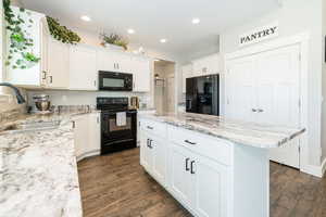 Kitchen with white cabinets, a kitchen island, a sink, and black appliances
