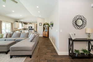 Living room with baseboards, vaulted ceiling, dark wood-type flooring, and recessed lighting