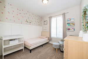 Bedroom featuring wallpapered walls, carpet, and a wainscoted wall