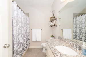 Hallway bathoom featuring curtained shower, tile patterned flooring, toilet, vanity, and baseboards