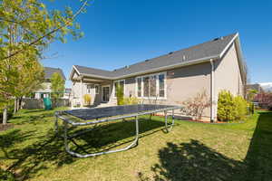 Back of house featuring a trampoline, a lawn, stucco siding, and fence