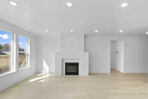 Unfurnished living room featuring baseboards, a glass covered fireplace, recessed lighting, and light wood-style floors