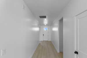 Corridor featuring baseboards, visible vents, and light wood-style flooring
