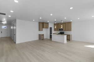 Kitchen with stainless steel microwave, baseboards, range, brown cabinetry, and open floor plan