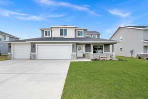 Prairie-style home featuring a front lawn, a porch, stone siding, concrete driveway, and a garage