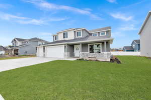 View of front of house with stone siding, covered porch, concrete driveway, fence, and a front yard