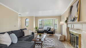 Living area featuring baseboards, crown molding, light tile patterned flooring, and a tiled fireplace