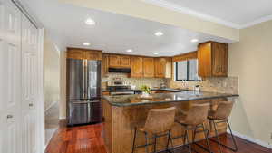 Kitchen featuring brown cabinetry, appliances with stainless steel finishes, baseboards, and under cabinet range hood