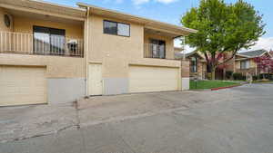Exterior space with stucco siding, an attached garage, driveway, and a balcony