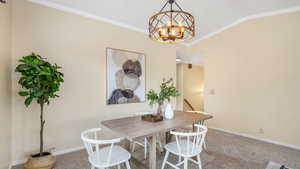 Carpeted dining room featuring vaulted ceiling, baseboards, crown molding, and a chandelier