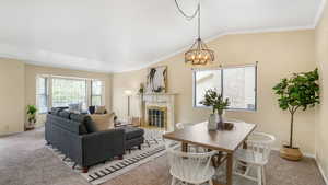 Living area with a fireplace with flush hearth, light carpet, vaulted ceiling, baseboards, and an inviting chandelier