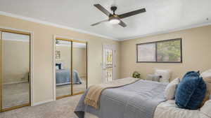 Bedroom with baseboards, light colored carpet, a ceiling fan, two closets, and ornamental molding