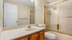 Bathroom featuring vanity, bath / shower combo with glass door, and toilet