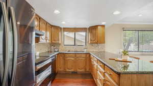 Kitchen with a sink, brown cabinetry, stainless steel appliances, dark wood finished floors, and a peninsula