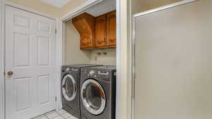 Clothes washing area featuring cabinet space, light tile patterned floors, and washer and clothes dryer
