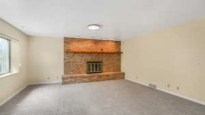 Unfurnished living room with a brick fireplace, carpet, visible vents, and baseboards