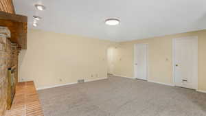 Unfurnished living room featuring baseboards, a brick fireplace, visible vents, and carpet flooring