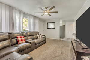 Living room with ceiling fan, baseboards, ornamental molding, and light carpet