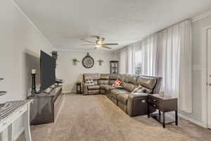 Living room with ceiling fan, light carpet, crown molding, and baseboards