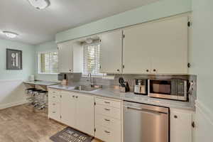 Kitchen featuring a sink, light countertops, a wainscoted wall, stainless steel appliances, and light wood-style flooring