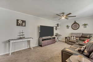 Living room featuring carpet floors, a ceiling fan, baseboards, and ornamental molding