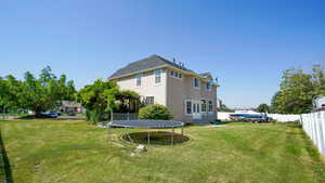 Rear view of house with fence, a lawn, stucco siding, and a trampoline