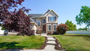 Traditional home featuring stone siding, a front yard, stucco siding, and fence