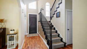 Foyer with baseboards, light wood-style flooring, a high ceiling, and stairs