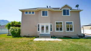 Rear view of house featuring stucco siding, fence, a yard, and french doors