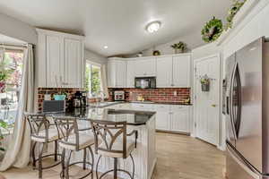 Kitchen featuring a peninsula, a sink, stainless steel fridge, dark countertops, and black microwave