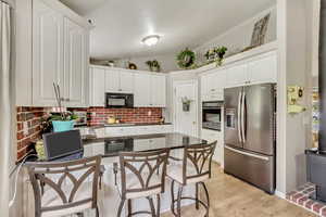Kitchen with stainless steel appliances, dark countertops, a peninsula, a breakfast bar area, and white cabinetry