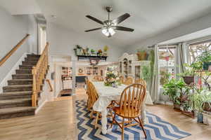 Dining space featuring stairway, ceiling fan, high vaulted ceiling, and light wood-style flooring