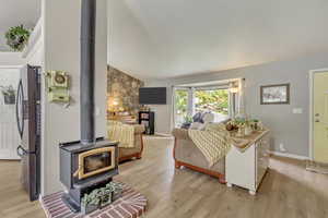 Living area featuring vaulted ceiling, baseboards, light wood-style floors, and a wood stove
