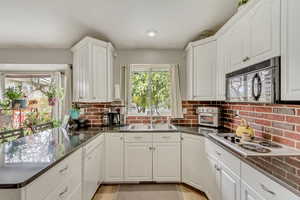 Kitchen with electric stovetop, a sink, white dishwasher, black microwave, and decorative backsplash