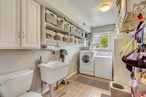 Clothes washing area with washing machine and clothes dryer, a textured ceiling, light tile patterned flooring, baseboards, and laundry area
