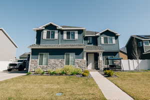 Craftsman-style home featuring fence, a shingled roof, a front lawn, and stone siding